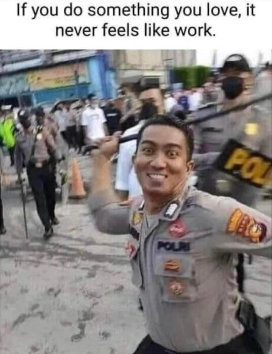 Glad polis tar selfie, oroligt bakgrundsfolk, text om kärlek till jobbet.