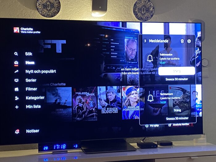 TV-skärm som visar en streamingtjänst med filmer och serier, popup-fönster med meddelanden, vid en vägg dekorerad med tallrik.