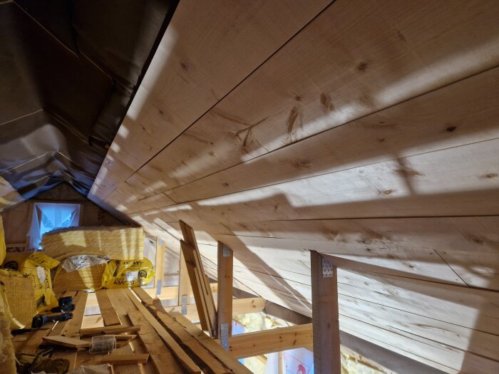 Inomhusbyggarbetsplats med träpanel, isoleringsmaterial och konstruktionselement synliga i takvinkel.