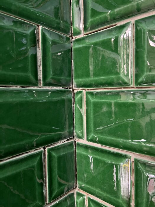 Gröna kakelplattor med glaserad yta och synlig fog, möjligen i ett kök eller badrum.