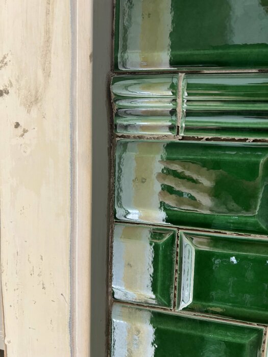 Gröna kakelplattor intill en beige vägg, makroperspektiv, detaljer av hantverk och fogmassa.