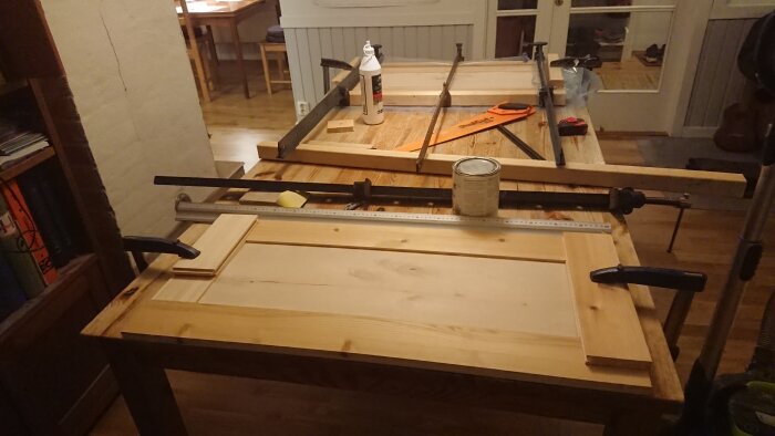 Snickeriprojekt med träplankor och verktyg på arbetsbänk i hemmiljö. Möjlig dörrtillverkning.