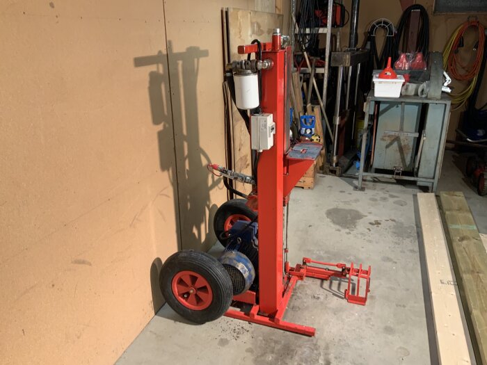 Ett rött däckbyteverktyg i en oorganiserad garageverkstad med verktyg och kablar på väggen.