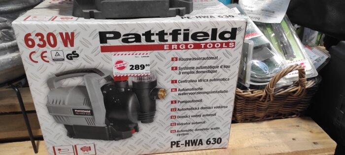 Förpackning för Pattfield automatisk vattenpump, 630W, flerspråkiga beskrivningar, röd prislapp, inomhusmiljö.