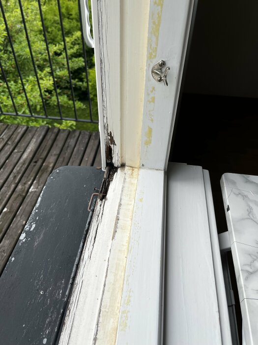 Sliten fönsterkarm med skadad färg och mögel vid en balkong, behöver reparation och ommålning.