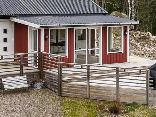 Rött hus med vit knut, veranda, glasdörrar, naturtomt.