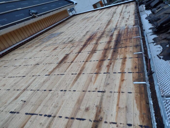 Ett tak under renovering med synlig träunderkonstruktion och takpannor vid sidan.