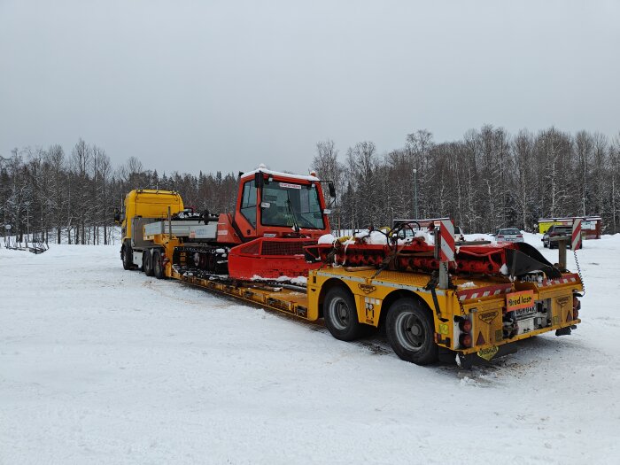 Lastbil med släp transporterar röd bandvagn, vinterlandskap, snö, skog i bakgrunden.