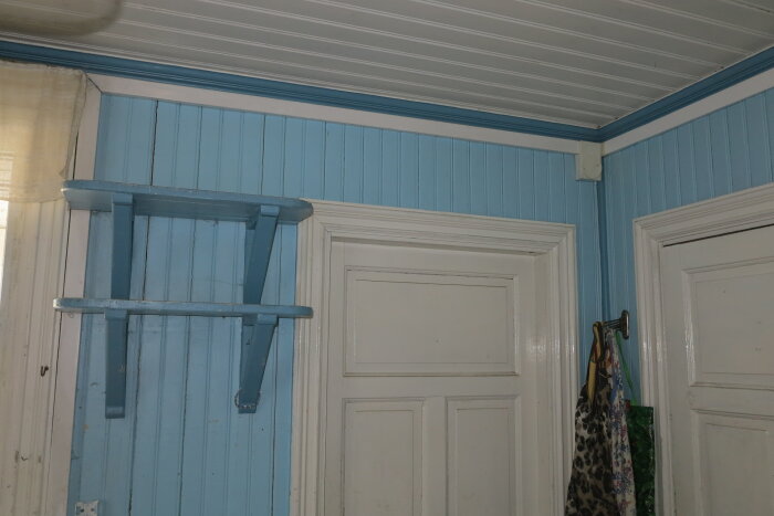 En hörna av ett rum med blå väggar, vit dörr, och upphängd stol.