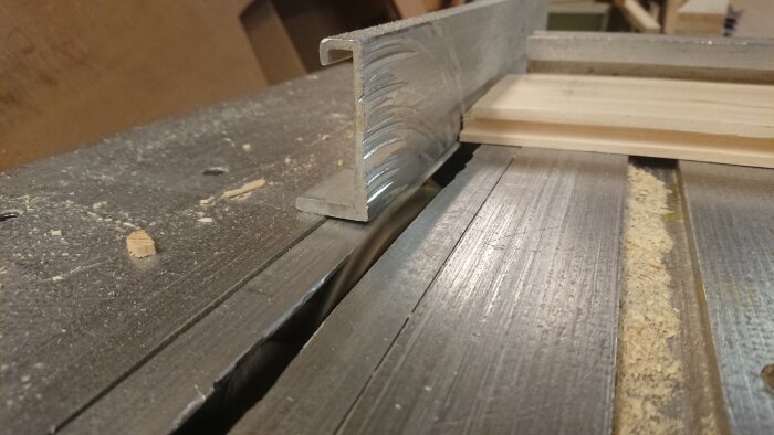 Metallprofil på ett sågat träbord med sågspån och träavfall. Arbetsyta för snickeri eller hantverk.