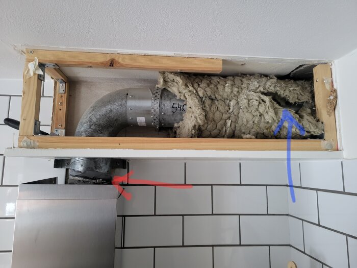 Uppriven vägg visar isolering och ventilation i ett kök, med rörmärkningar på en vent.