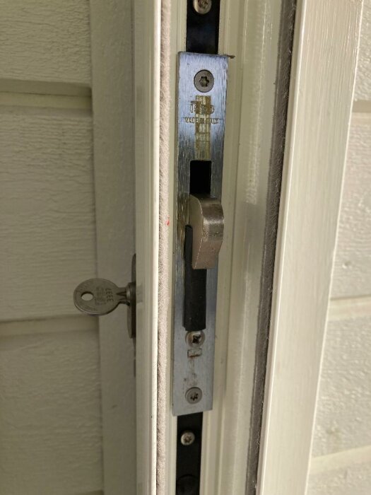 Dörr med synlig låsmekanism, säkerhetslås, nyckel i låset, vit dörrkarm och metallskåra.