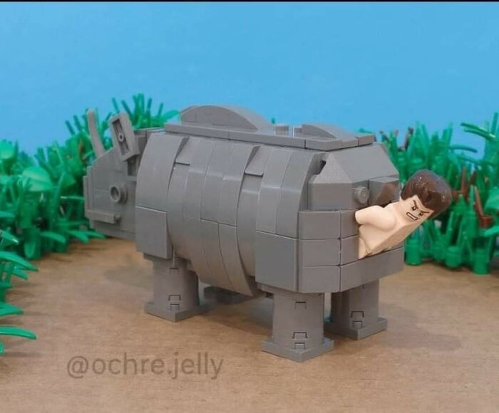 Lego-figur inuti byggd Lego-noshörning på en grön bakgrund av plastväxter.