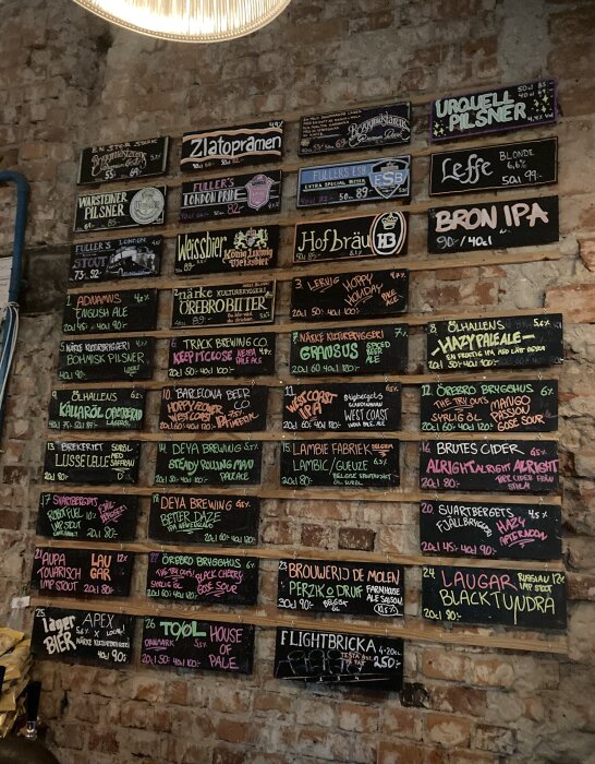 Ölmeny på en vägg med många olika ölsorter och priser skrivna på svarta skyltar.
