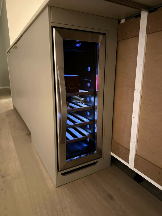 Inbyggd vinkylskåp med glasdörr, trähyllor, integrerat i ljust kök, digital temperaturvisning upplyst i blått.