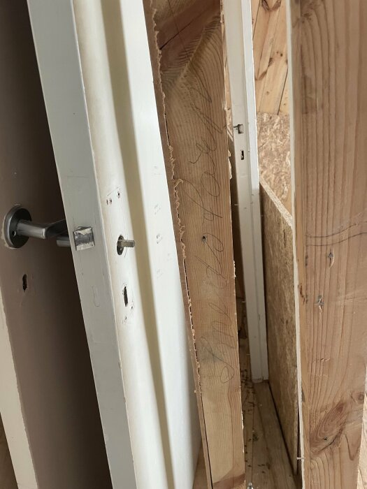 Delvis demonterad dörrkarm och ocistade träplankor, pågående konstruktions- eller reparationsarbete, inomhusmiljö.
