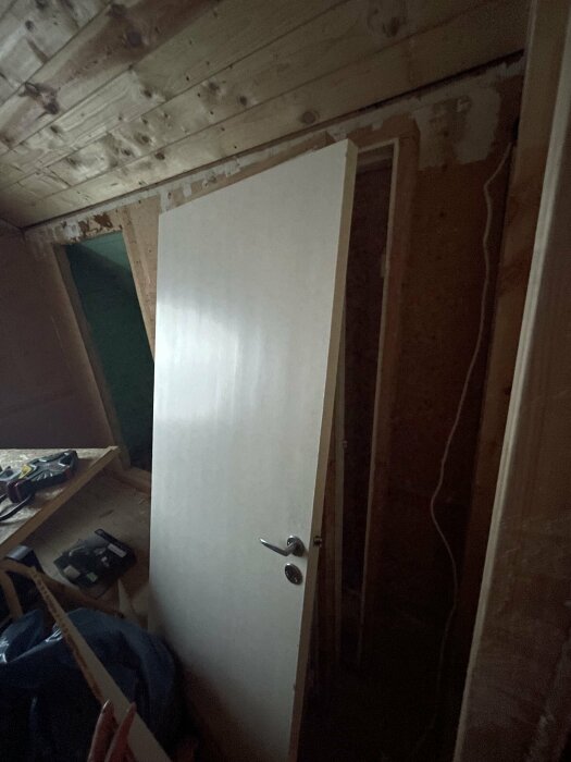 Ej färdigställd inomhusmiljö med en lös vit dörr lutad mot en vägg, arbetsmaterial synliga.