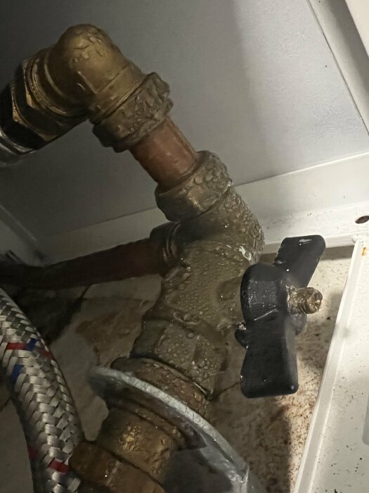 Rostig vattenledning med kondens och svart vred, möjligen i ett underhållsutrymme eller krypgrund.