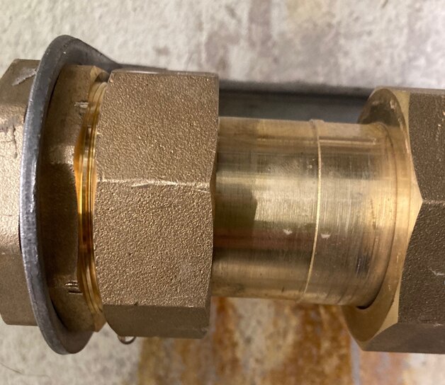 Mässingsrör med koppling och packning mot en grå och brun bakgrund. Industriellt, VVS-relaterat, närbild.