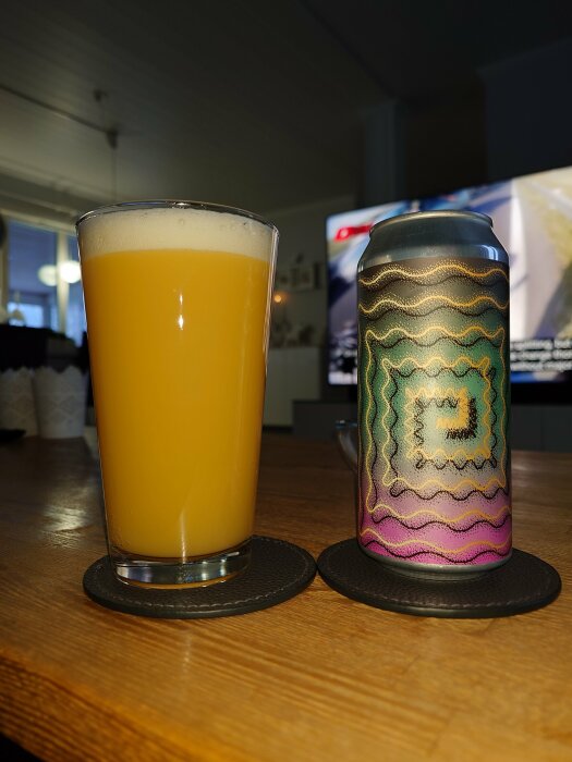 Ett glas med gul vätska och skum ovanpå bredvid en färggrann burk på träyta.