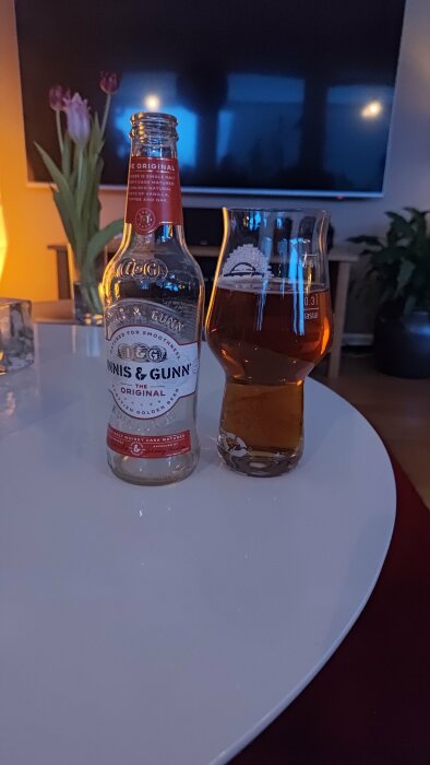 Ölflaska och glas på bord, mysig inomhusmiljö, diffust ljus, skymning, avslappnad atmosfär.