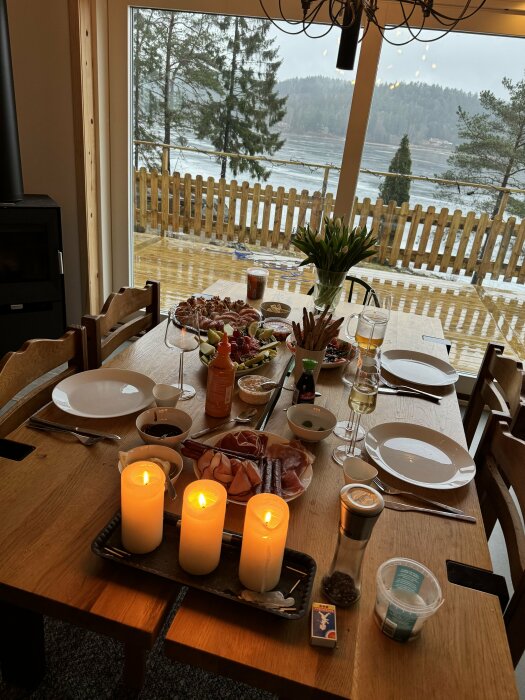 Mysig middag, dukat bord med delikatesser, tända ljus, skymt av sjölandskap utanför, inbjudande och hemtrevlig atmosfär.