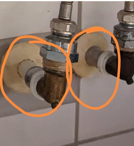 Rörkopplingar med korrosion markerade med orange cirklar på en kakelvägg.
