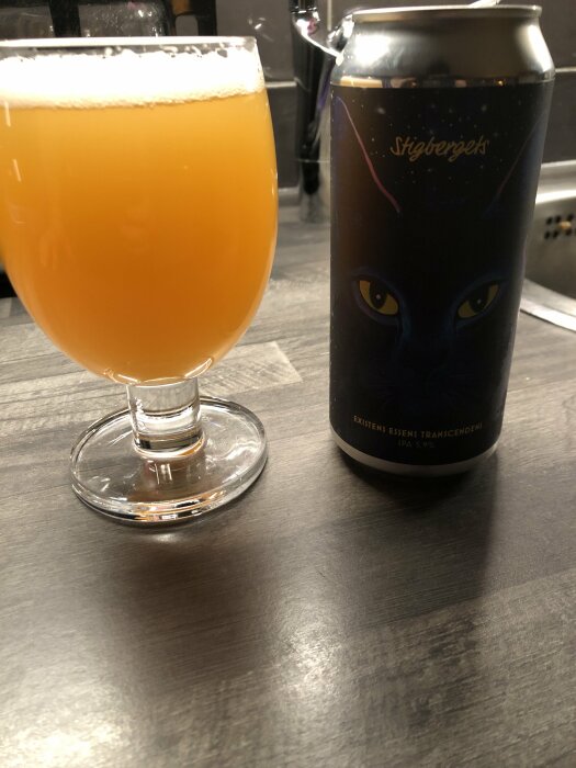 Ölglas på fot fylld med grumlig dryck, burk med kattögon, mörk yta.