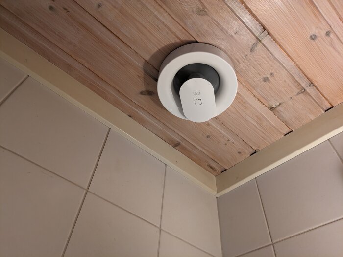 Takmonterad ventilation i träklädd hörna med kakelvägg. Modern, enkel design.