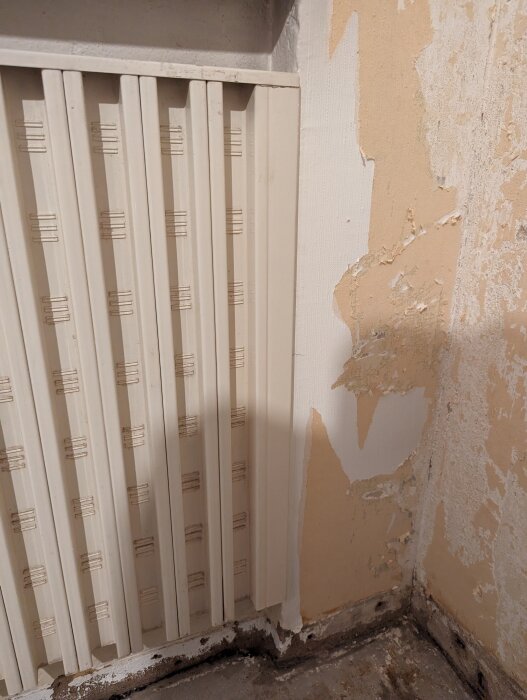 Värmeelement vid skadad vägg och golv i behov av renovering.
