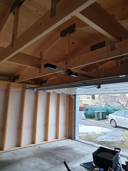 Tomt garage, träbjälkar i taket, isolering på väggar, öppen port, dagtid, utsikt mot bostadsområde.