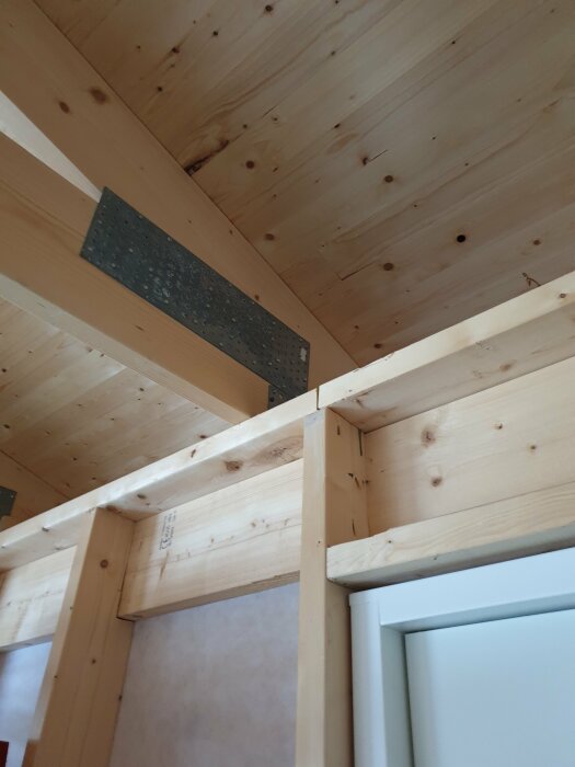Träbjälklag med oisolerad träspånskiva monterad ovanför dörrkarm i byggnad under konstruktion.