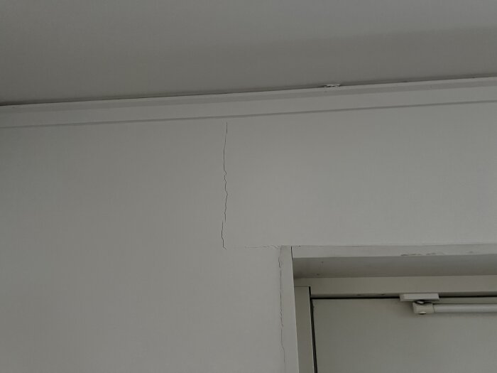En vit vägghörn med en synlig spricka och en gardinstång ovanför en dörrkarm.