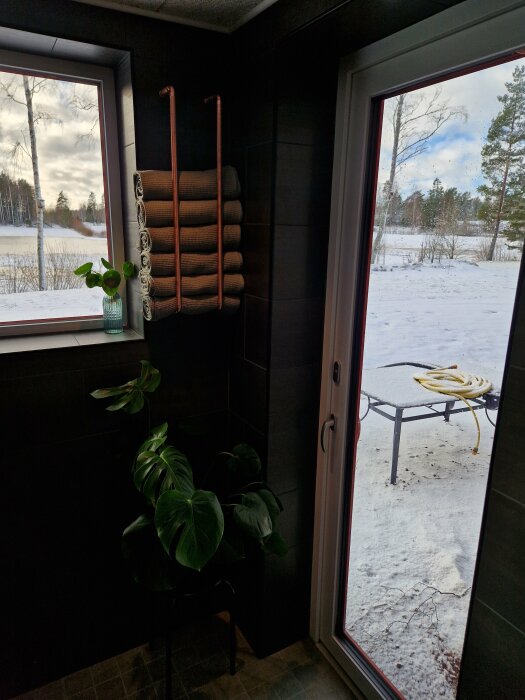 Inomhus med utsikt mot snötäckt natur, handdukar, gröna växter, glasvas, modern inredning, känsla av lugn.