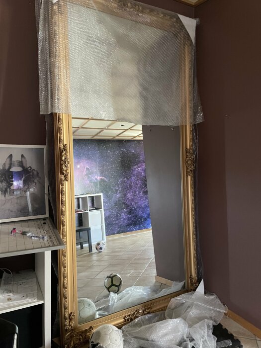 Stor spegel med bubbelplast, rum reflekteras med kosmisk tapet och fotbollar på golvet.