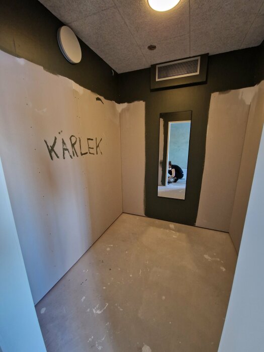 Ett omålade rum, ordet "KÄRLEK" på väggen, spegelbild av person som fotograferar.