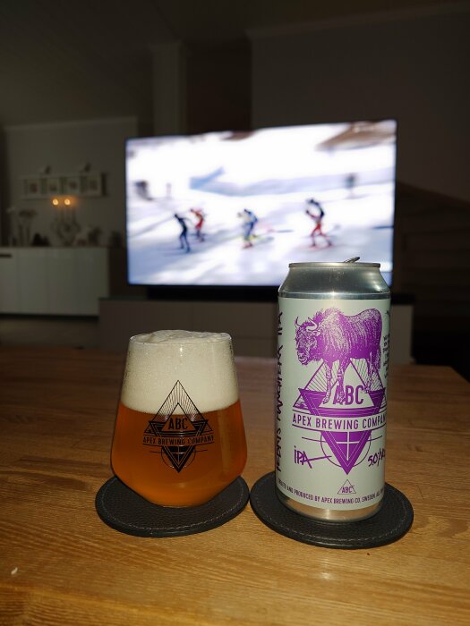 Ett ölglas och burk från Apex Brewing Company framför oskarp TV med skidtävling.