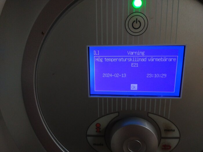 Digital display med felmeddelande, varningsikon, datum, tid, ok-knapp. Rund grå kontrollenhet nedanför.