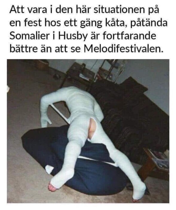 Person, klädd i vit dräkt, fastnar i en soffa, humoristisk situation.