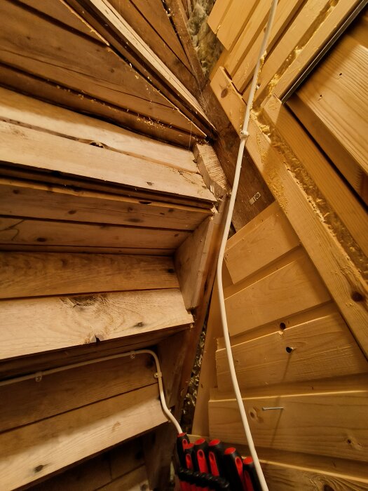 Inredning av trä, lutande tak, skruvdragare, isolering synlig, elektrisk kabel, byggnadsarbete eller renovering pågår.