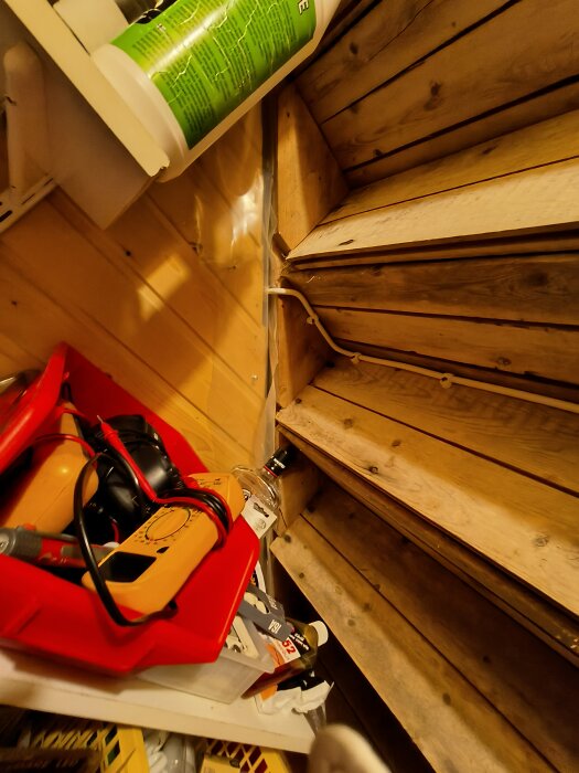 Oorganiserat utrymme med verktyg, flaskor och föremål i trähytt. Bilden är tagen i en vinklad position.