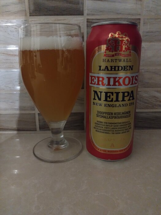 Ölglas bredvid burk av Hartwall Lahden Erikois NEIPA, mönstrad yta, skumkrona, disig dryck.