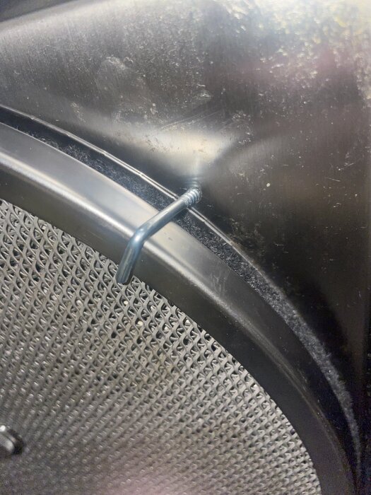 En blå kabel zip-tied till ett metallgaller, mot en svart plastbakgrund med damm och smutsansamlingar.