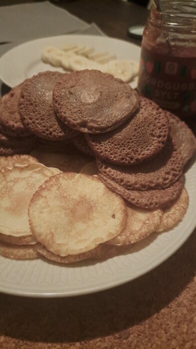 Ett fat med pannkakor och sirap, några skivade bananer i bakgrunden. Hemlagad, dessert eller frukost. Hygglig atmosfär.