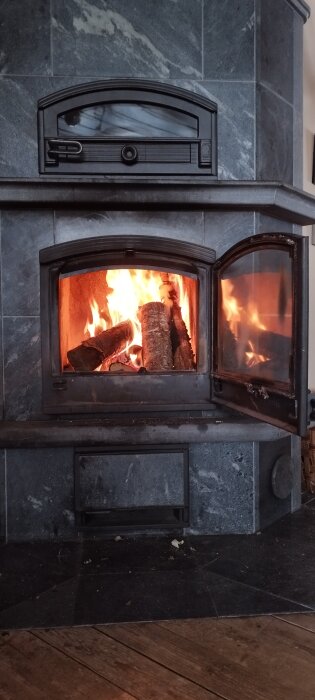 Kamin med öppna dörrar brinner ved, stenomramning, hemtrevlig och varm atmosfär.