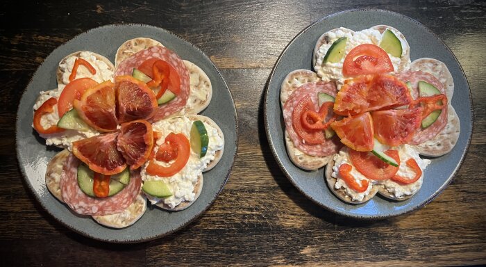 Två tallrikar med knäckebröd och pålägg som salami, tomat, gurka och fikon.