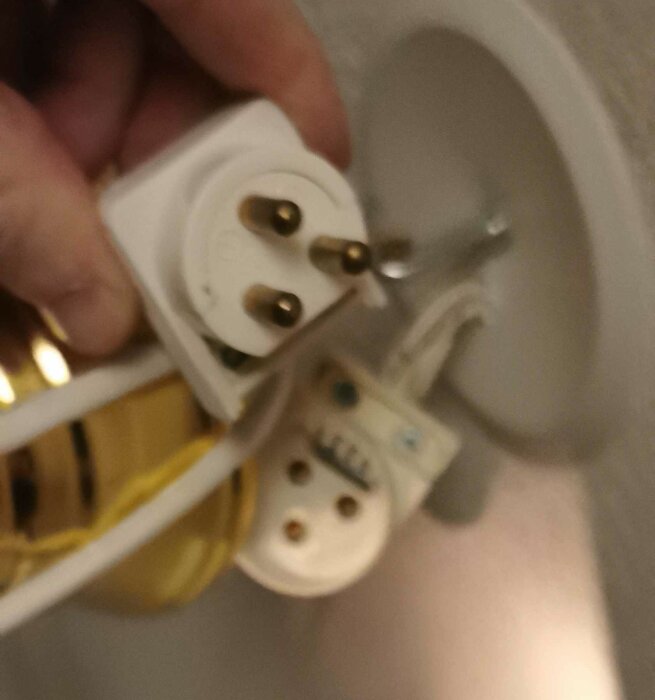 En hand håller en oskarp bild av en vit elkontakt framför ett handfat.