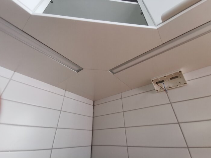 Vitt kakel, taklampan är borttagen, kablar synliga, ljust rum.