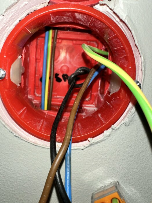 Öppen elektrisk låda med kablar i väggen, installationsarbete pågår, ofärdigt, säkerhetsrisk.