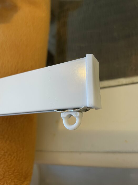 Vit gardinstång och gardinhakar nära ett fönster med gult gardintyg.
